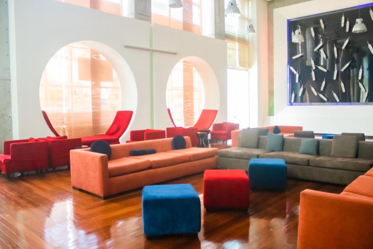 Decapolis Hotel Panama City Exterior photo The photo depicts a modern and stylish lounge area. It features a combination of colorful seating arrangements, including a long, orange sofa and various cubes in blue and red, creating a vibrant atmosphere. There are also two red lounge chairs with 