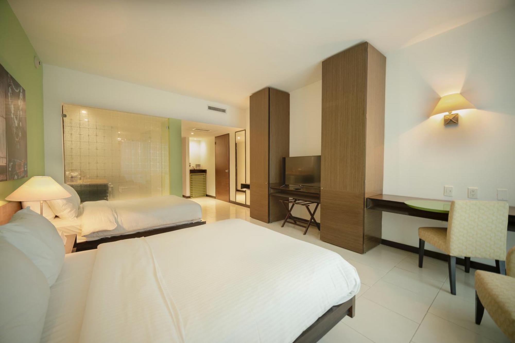 Decapolis Hotel Panama City Exterior photo The photo shows a modern hotel room featuring two beds with white bedding. There is a large window allowing for natural light, and one wall is occupied by built-in cabinets and a flat-screen TV. A small desk with a chair is positioned near the TV, an